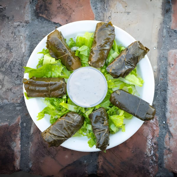 Six dolmades on a bed of lettuce with a side of tzatziki sauce on a white plate.