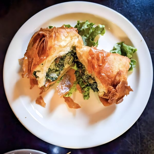 A golden-brown spanakopita, cut in half to reveal a spinach and feta filling, on a white plate.