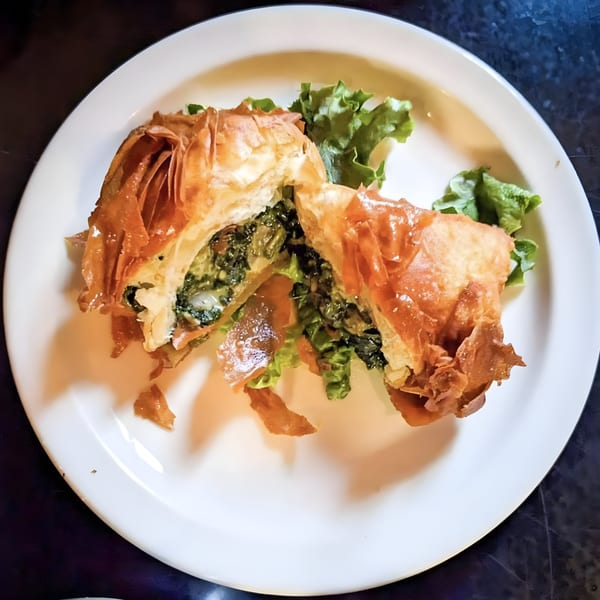 A golden-brown spanakopita, cut in half, revealing a savory spinach and feta filling on a white plate.