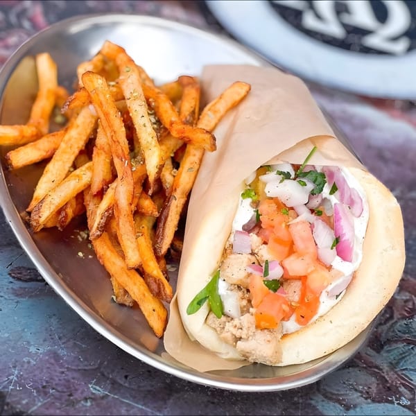 A Mediterranean gyro with chicken, tomatoes, onions, and sauce, served with seasoned fries on a metal plate.