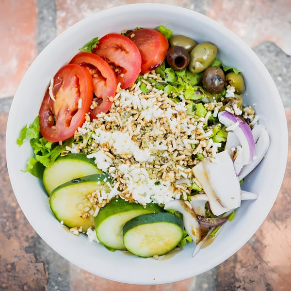 Overhead view of a Mediterranean salad with tomatoes, cucumbers, olives, feta, and crispy noodles.