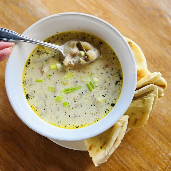 Creamy Mediterranean soup with green onions and spices, served with pita bread on a wooden table.