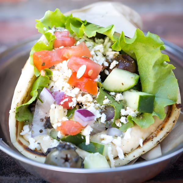 A Mediterranean pita wrap overflowing with fresh lettuce, tomatoes, cucumbers, feta, and olives.