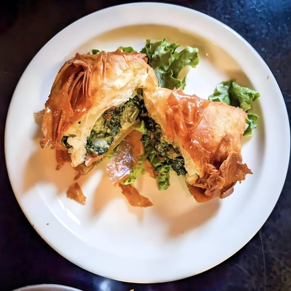 A golden-brown spanakopita, cut in half to reveal a spinach and feta filling, on a white plate.